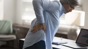Trabajador sujetándose la espalda baja por dolor de espalda después de cargar peso durante una jornada laboral.