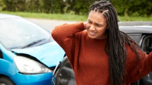 Persona sujetándose el cuello y la espalda después de un accidente automovilístico debido a lesiones musculares y dolor tardío.