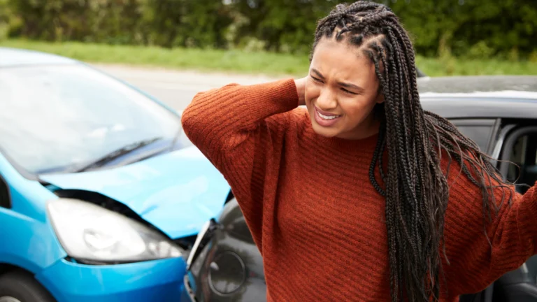 Persona sujetándose el cuello y la espalda después de un accidente automovilístico debido a lesiones musculares y dolor tardío.